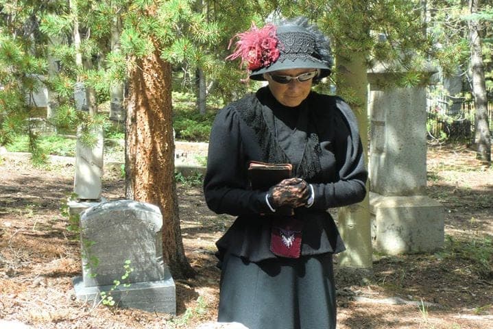 A Cemetery Crawl reenactor in a black Victorian mourning dress and plumed hat among headstones
