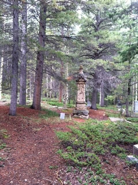 A carved sandstone obelisk monument in a pine forest cemetery