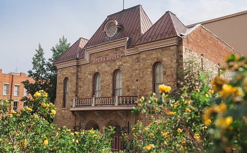 The Central City Opera House: a stone facade with an Opera House sign, framed by yellow roses
