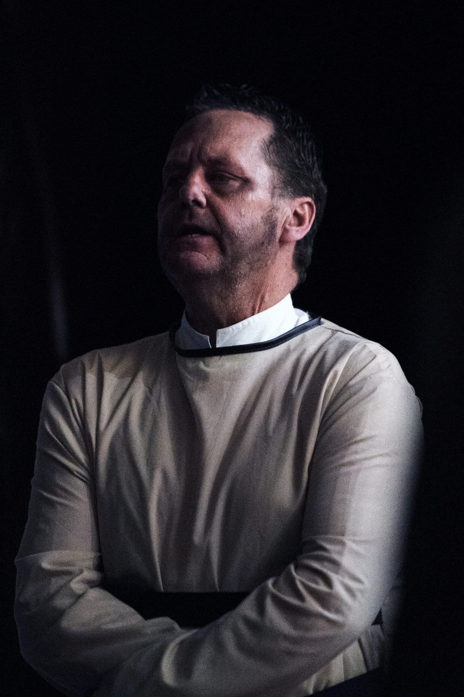 A Creepy Crawl guide in a pale period shirt, eyes closed, spot-lit against black