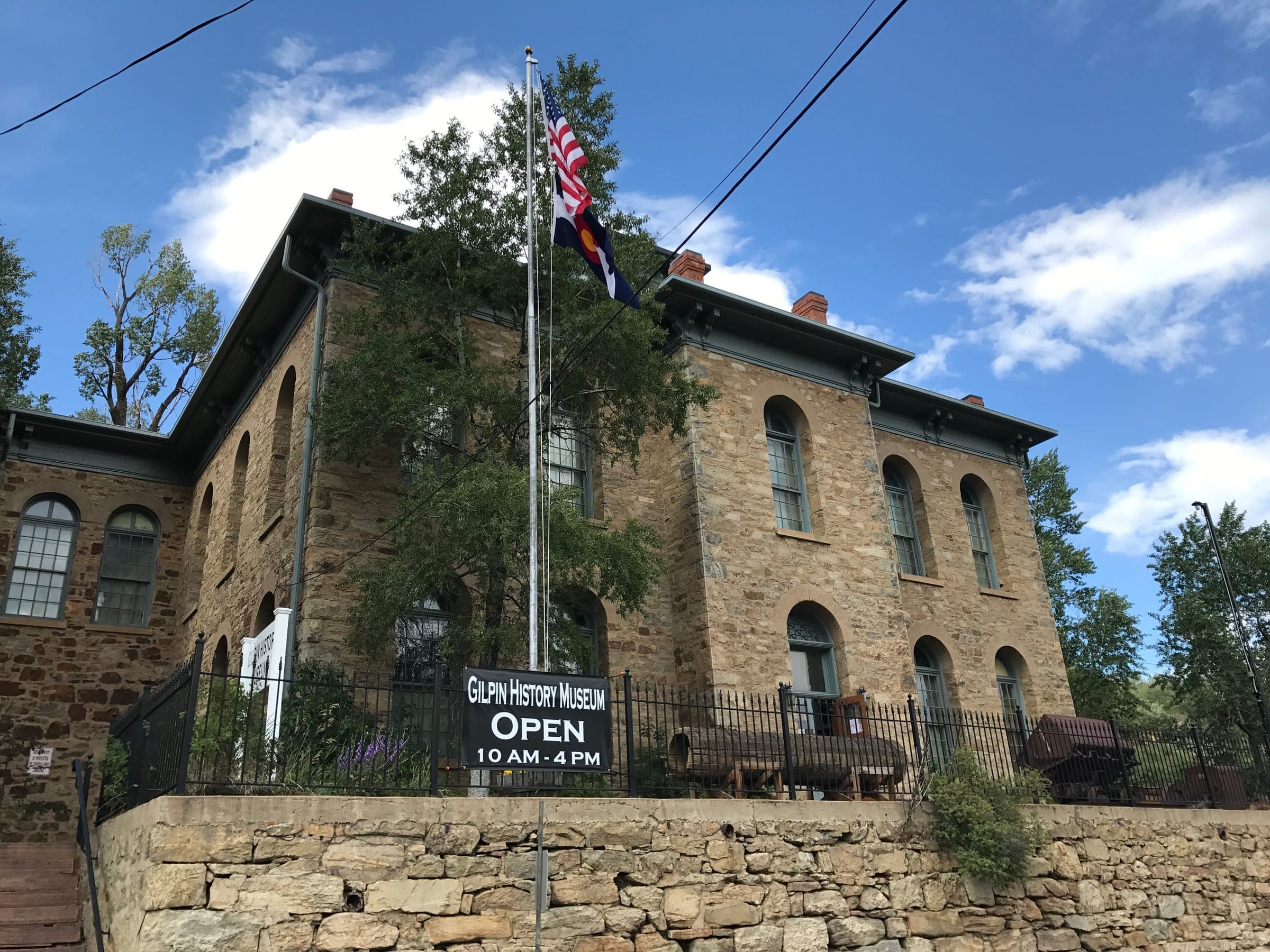 The Gilpin History Museum, a two-story stone schoolhouse with arched windows, flags and an open banner