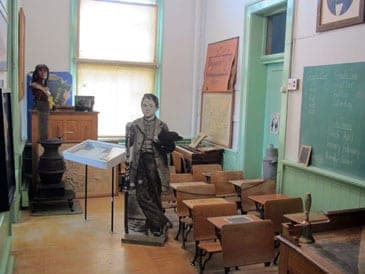 The recreated schoolroom: wooden desks, a chalkboard, a potbelly stove and a cut-out schoolboy