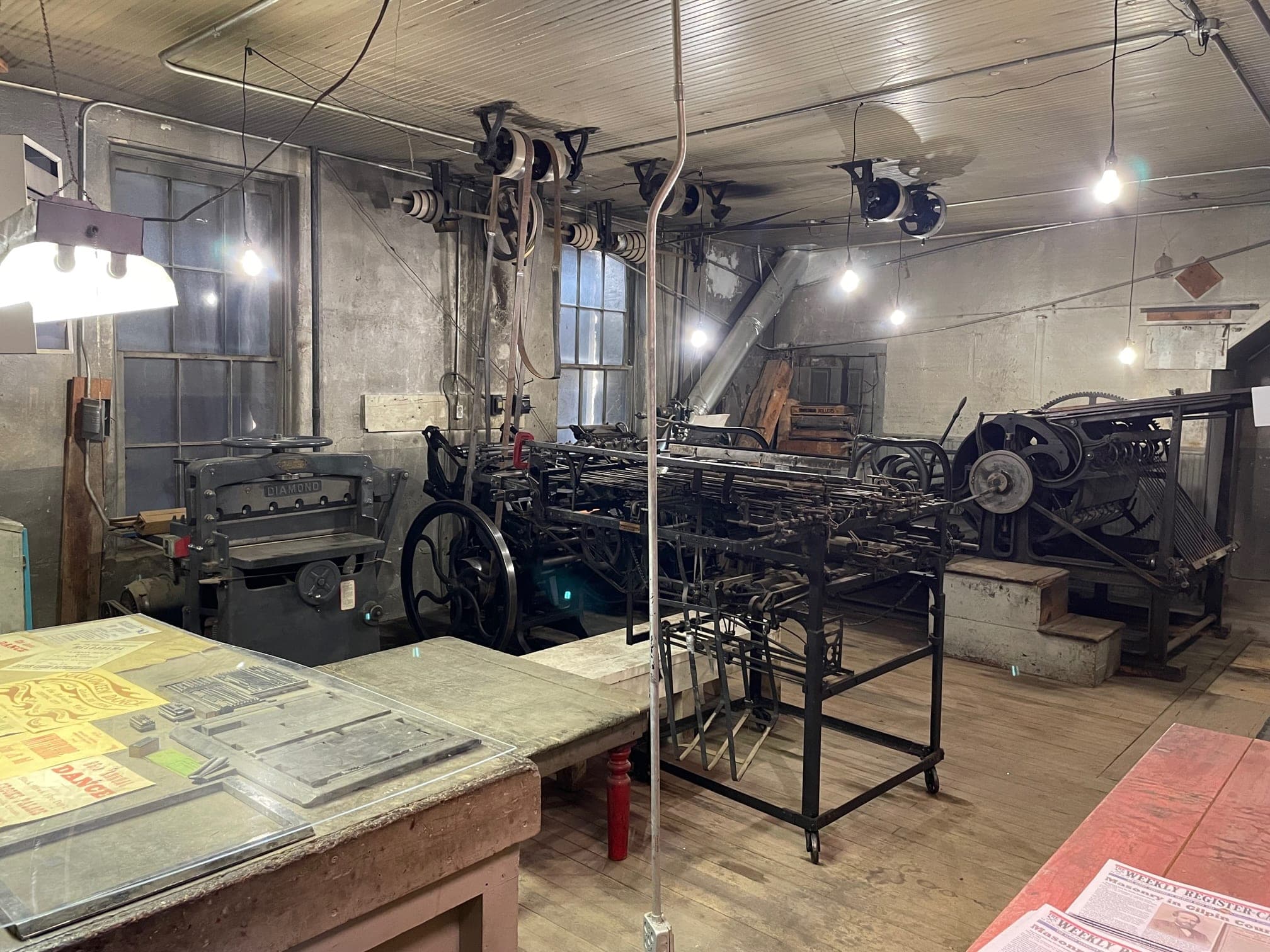 Inside the Weekly Register-Call print shop: a Chicago Taylor press, a Diamond paper cutter and belt-driven line shafts under bare bulbs
