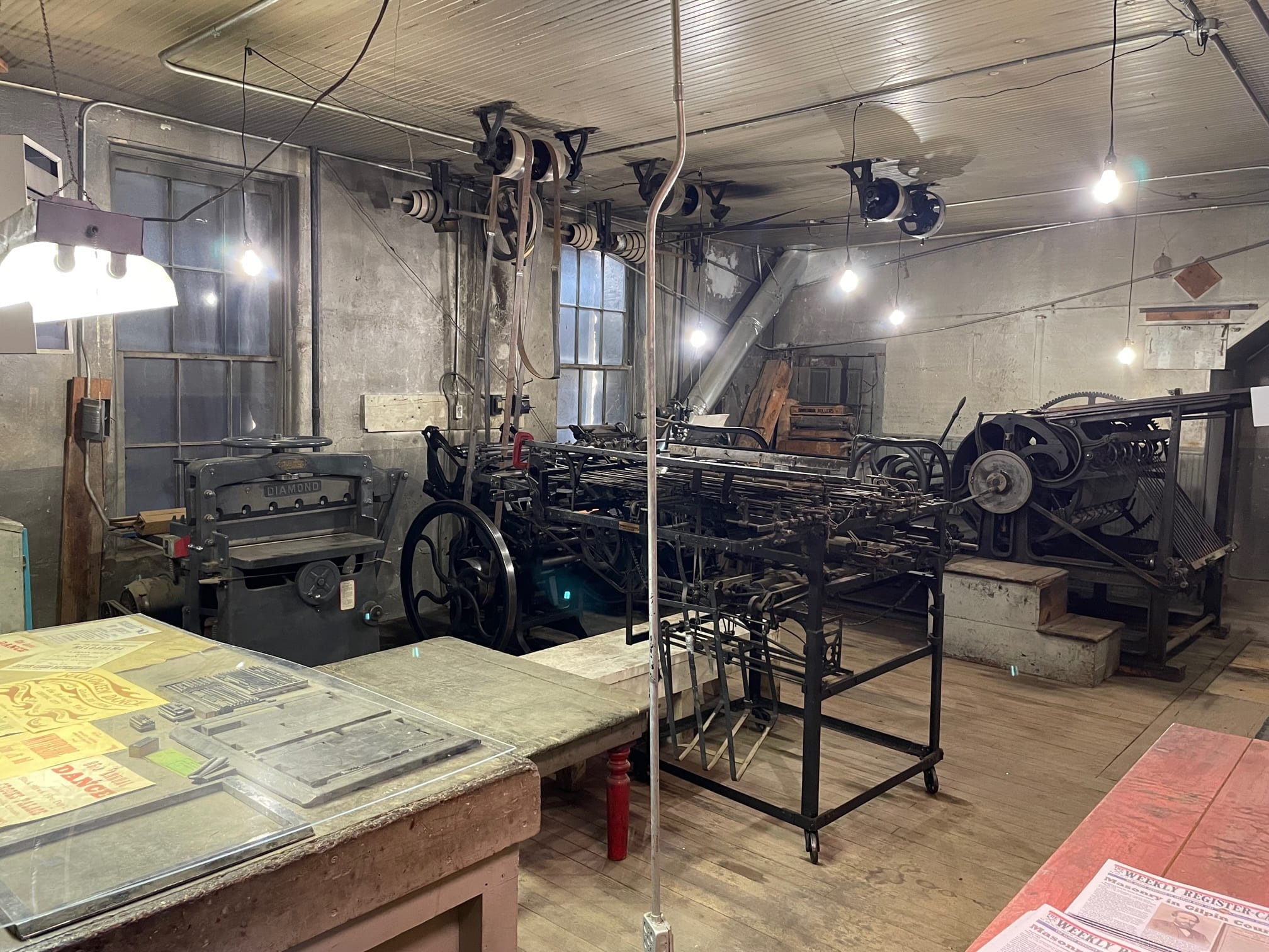 Inside the Weekly Register-Call print shop: a Chicago Taylor press, a Diamond paper cutter and belt-driven line shafts under bare bulbs