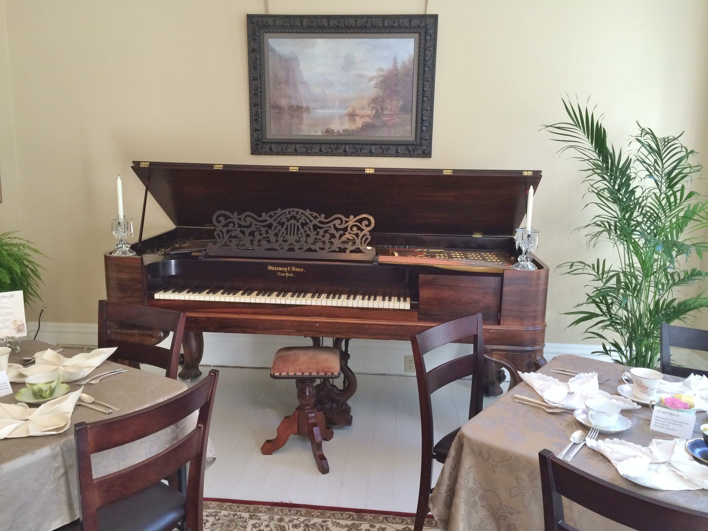 An 1865 Steinway square grand piano with its lid open under a framed landscape painting