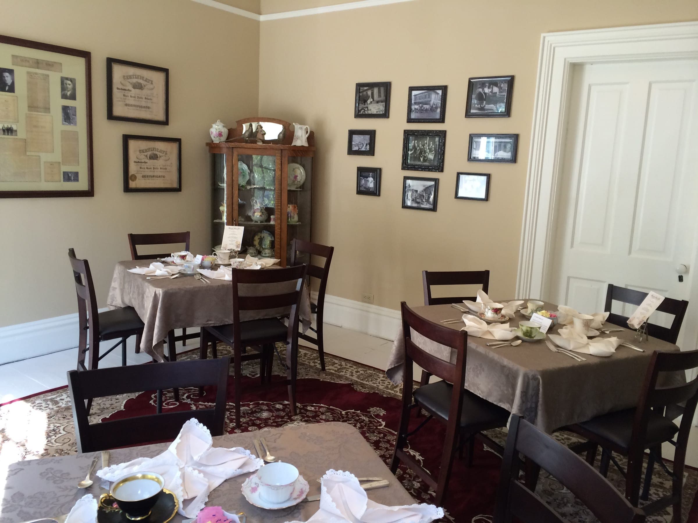 Tea tables beside an oak curio cabinet of china, with framed certificates and historic photographs
