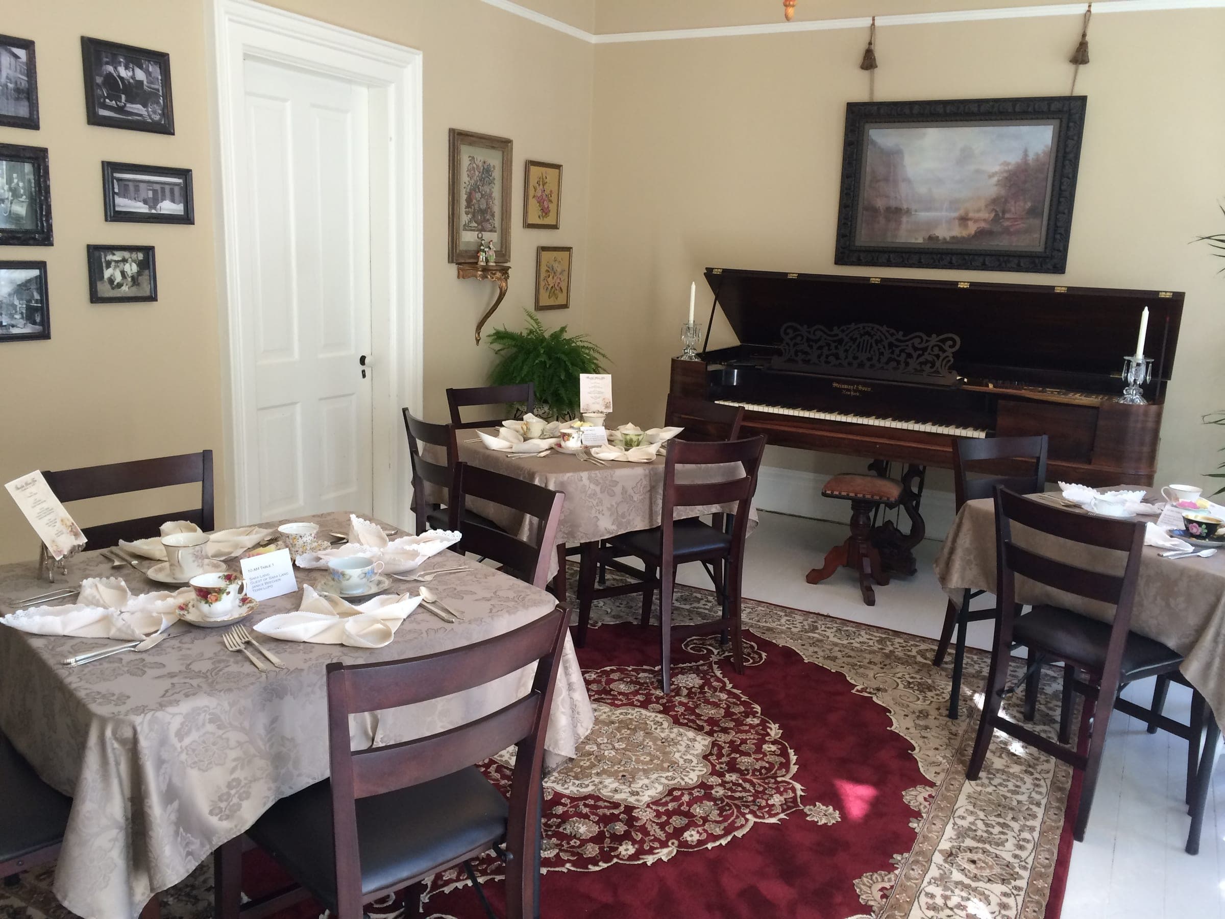 Tea tables on a red Persian rug beside the square grand piano and a wall of framed historic photographs