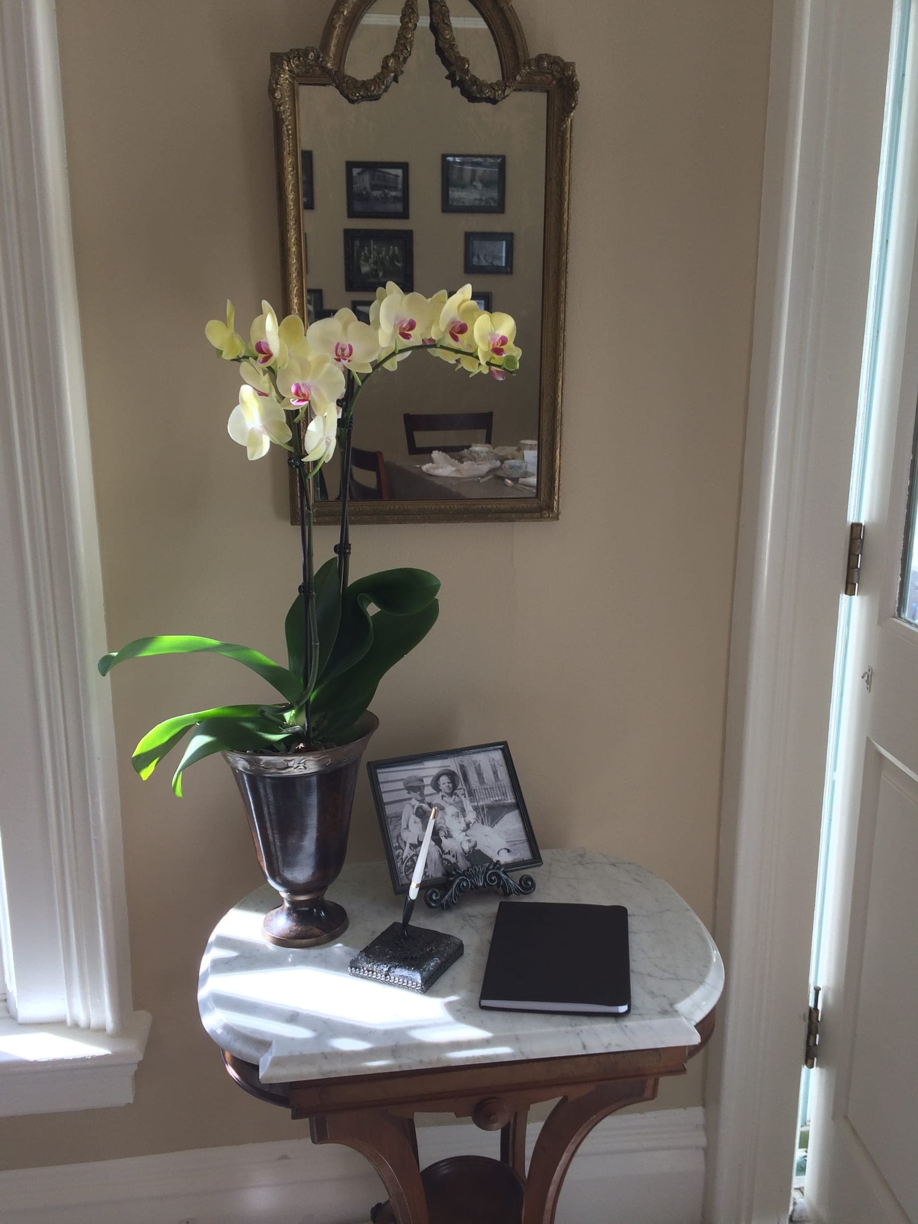 A yellow orchid, a gilt mirror, a framed photograph and a guest book on a marble-top table
