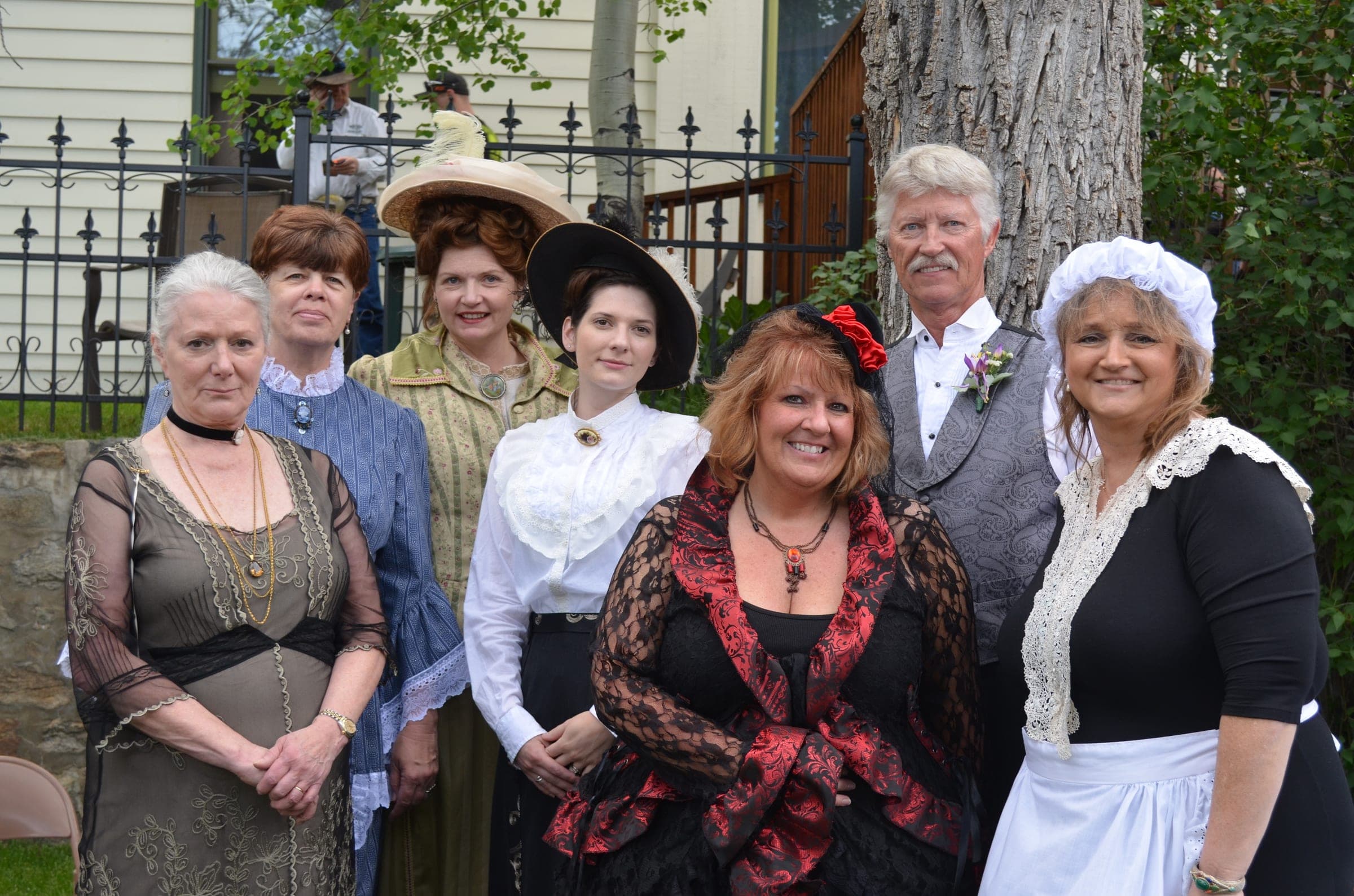Seven Gilpin Historical Society volunteers in Victorian and Edwardian costume outside by an iron fence