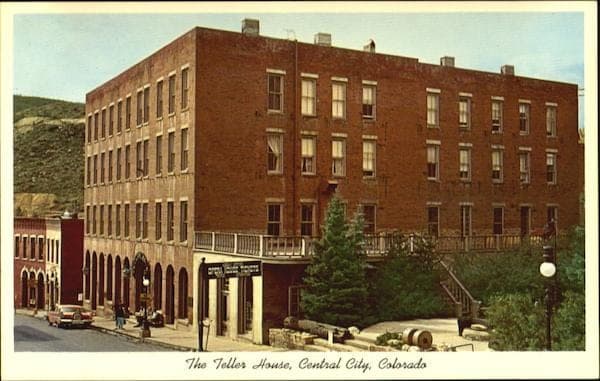 A vintage postcard of the Teller House, a four-story brick hotel with a balcony, with a 1950s car on the street