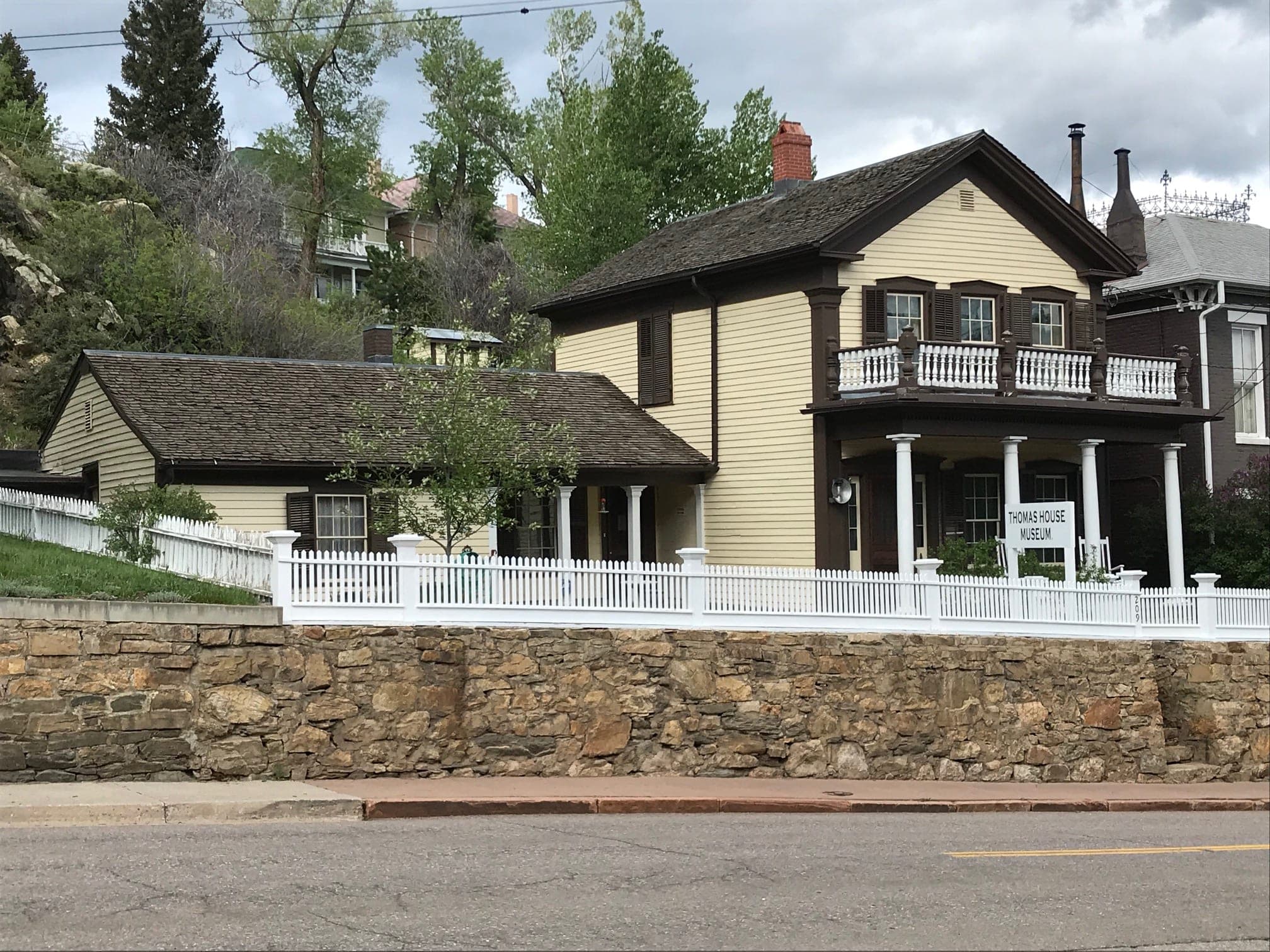 The Thomas House, a cream frame house with brown trim and a balcony behind a white picket fence