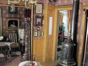 The parlor with an ornate parlor stove, patterned wallpaper and period portraits