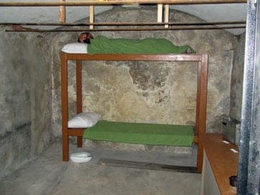 The old county jail cell: stone walls and a wooden bunk with a mannequin prisoner