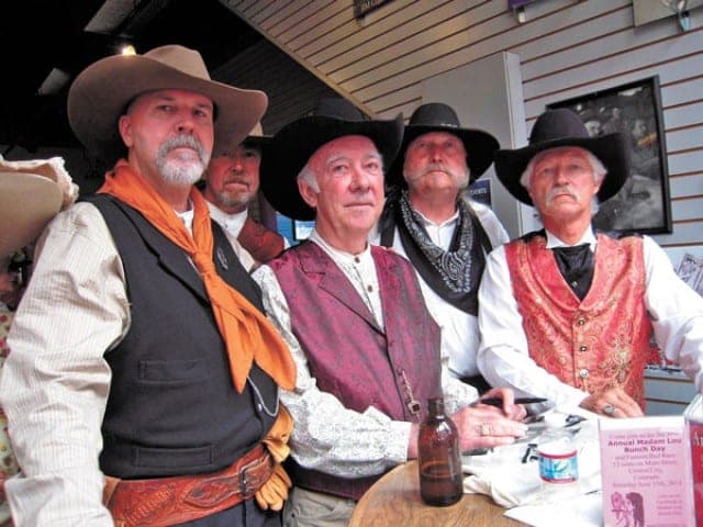 Five Wild Bunch members in hats, vests and bandanas around a table indoors
