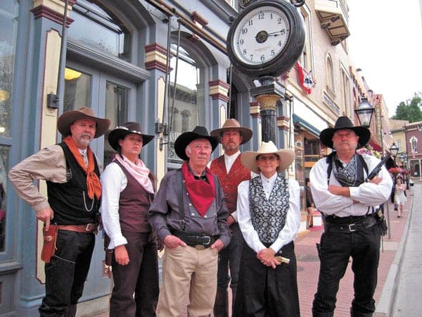 Seven Colorado Wild Bunch reenactors in Old West costume posed under the Main Street clock